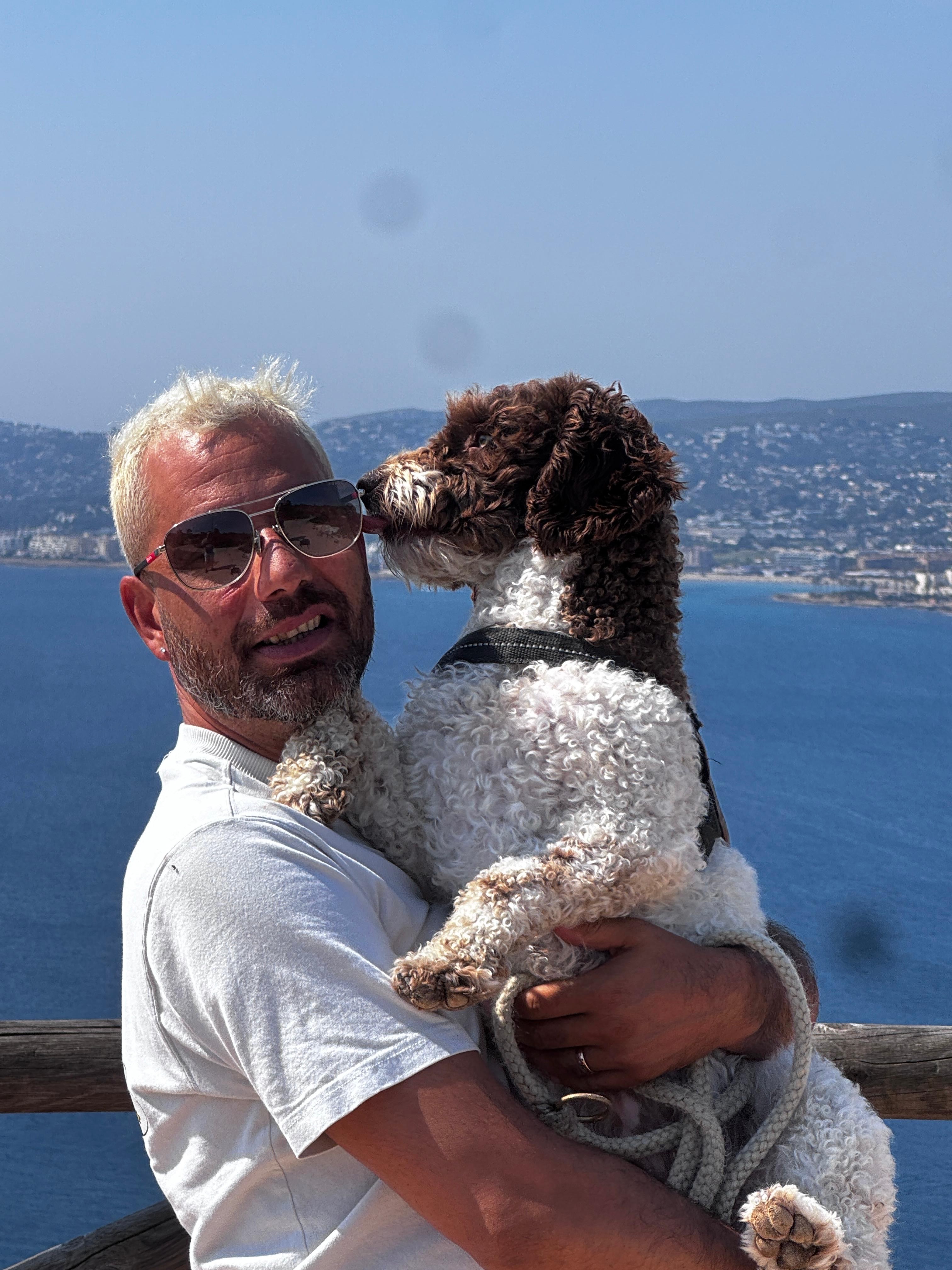 Marek holding his curly brown-and-white dog beside the sea